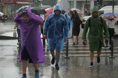 Bucharest, Romania - June 18, 2021: Foreign tourists cross the street in Piata Unirii, in heavy rain weather, in Bucharest, Romania. This image is for editorial use only.