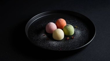 Siyah tabakta pudra şekeriyle tozlanmış küçük, renkli tatlı mantarları..