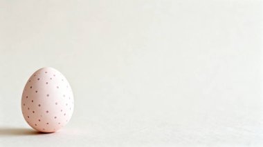 Tarafsız beyaz bir yüzey üzerinde duran elle boyanmış kırmızı noktalarla süslenmiş şirin pembe bir yumurta..