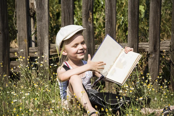 Boy reading a book near a wooden fence — Stock Photo, Image