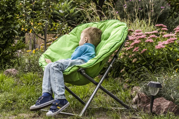 Menino dorme em uma cadeira no jardim — Fotografia de Stock