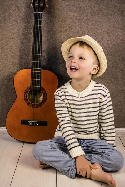 A boy and a stringed wooden guitar standing on the floor — Stock Photo, Image