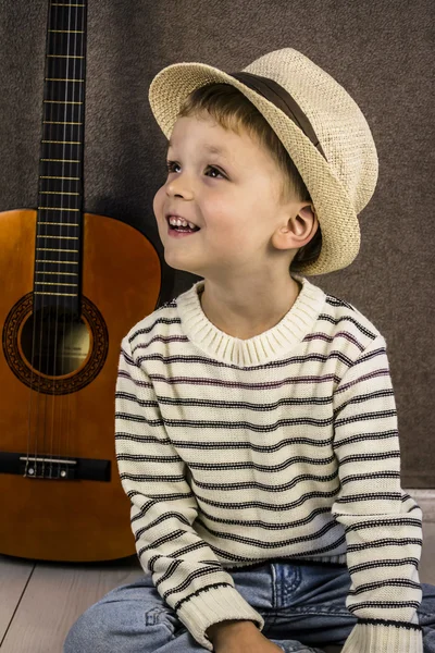 A boy and a stringed wooden guitar standing on the floor — Stock Photo, Image