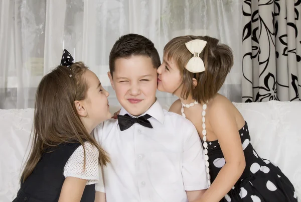 Две маленькие девочки целуют красивого мальчика — стоковое фото
