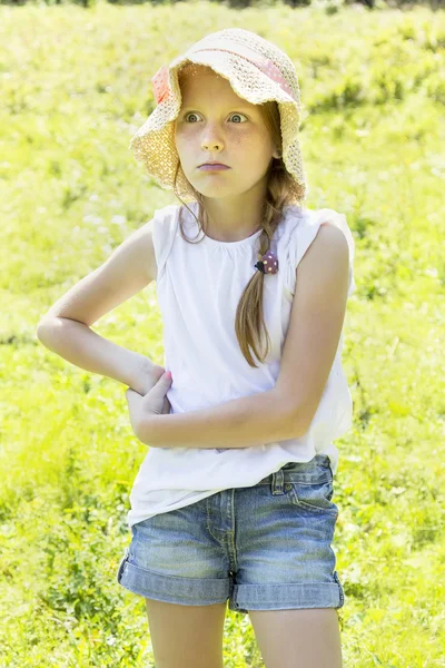 Flicka i en sommar hatt står på ängen — Stockfoto