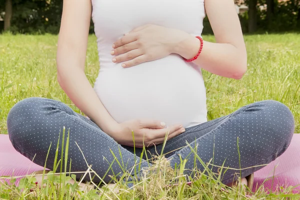 Donna incinta seduta in posizione di loto e meditando — Foto Stock