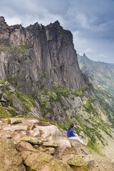 年轻女子坐在一个岩石与背包上和在眺望远方 — 图库照片