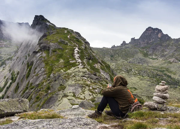 Молодая женщина сидит на скале с рюкзаком и смотрит на горизонт — стоковое фото