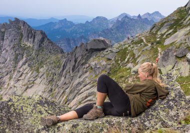 sırt çantası ile bir kayanın üzerine oturmuş ve ufuk arayan genç bir kadın