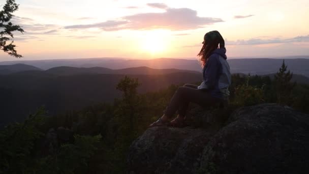 Meisje reiziger met rugzak zittend op het strand genieten van uitzicht op zee bij zonsondergang — Stockvideo