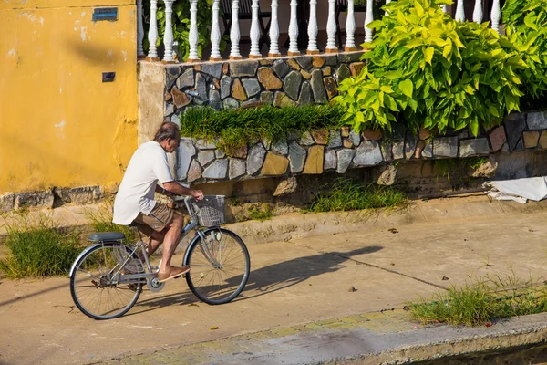 Viejo montando una bicicleta en asfalto camino hacia el cielo soleado puesta de sol — Foto de Stock