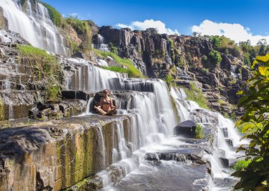 Pastoral tropik şelale yanında oturan Bikini kız