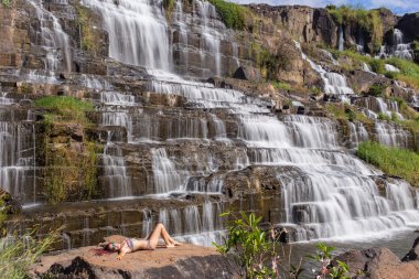 Pastoral tropik şelale yanında oturan Bikini kız