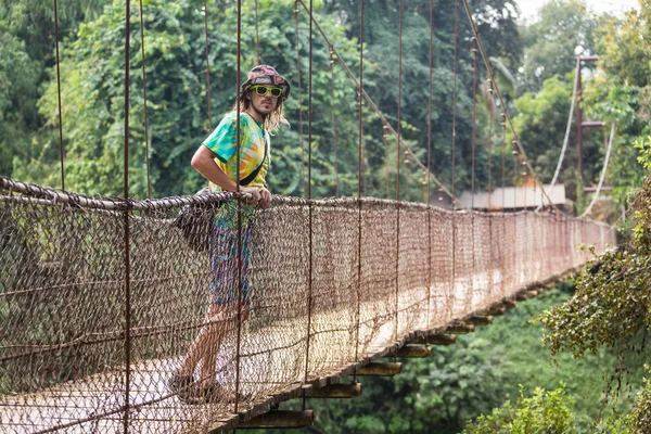 Traveling man crossing through hanging bridge in good sunny day over the lake — Stock Photo, Image