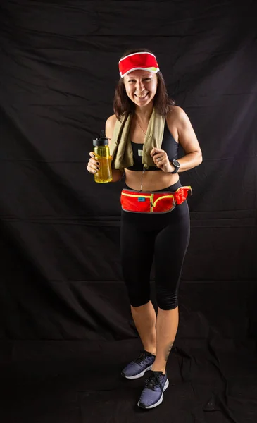 Menina bonita em jogging uniforme vermelho, bebe água após o treinamento no estúdio em um fundo preto — Fotografia de Stock