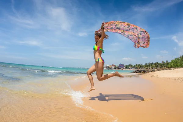美丽的女人，跑步和跳跃在沙滩上用彩色的组织 — 图库照片