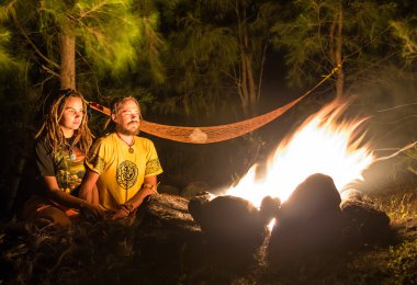 Çift oturan kayalık bir plajda kamp ateşi