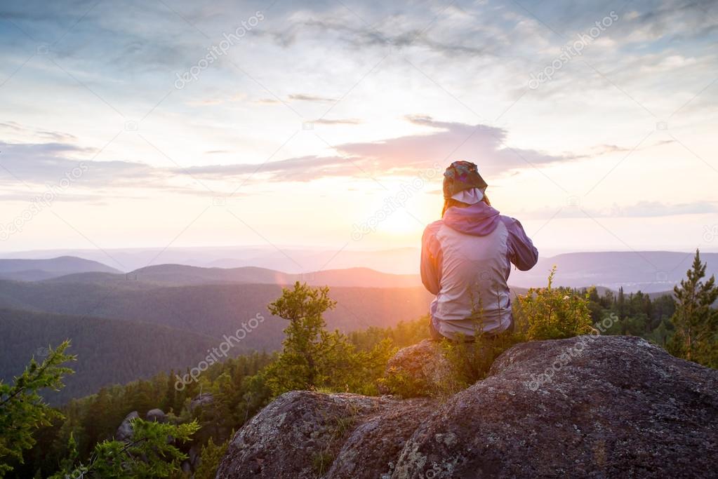 Young woman sitting on a rock, looking to the horizon