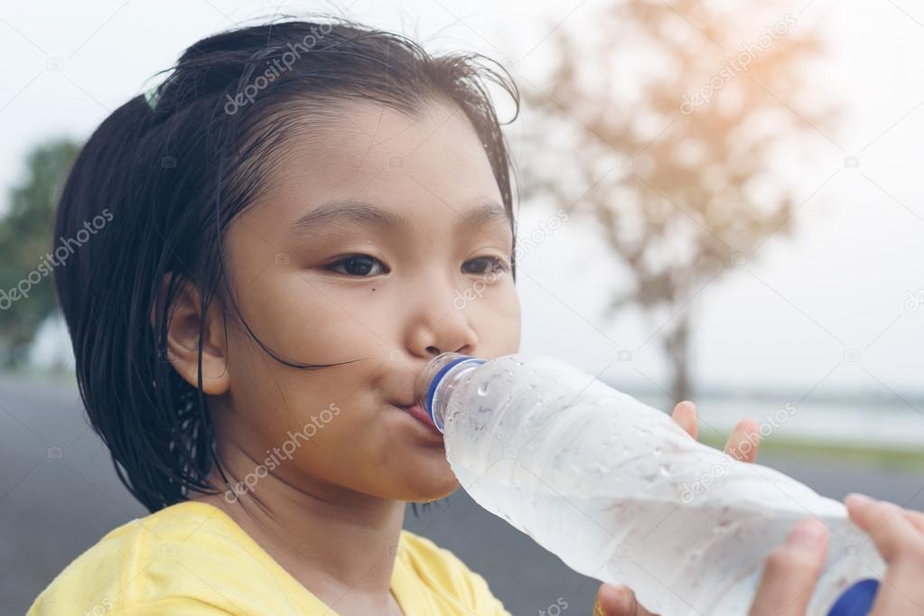 Cute girl is drinking water from plastic bottle. Clean water wil