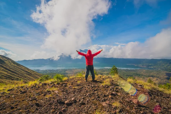 Joven de pie con las manos levantadas en la cima de una montaña y disfrutando de la vista del valle — Foto de Stock