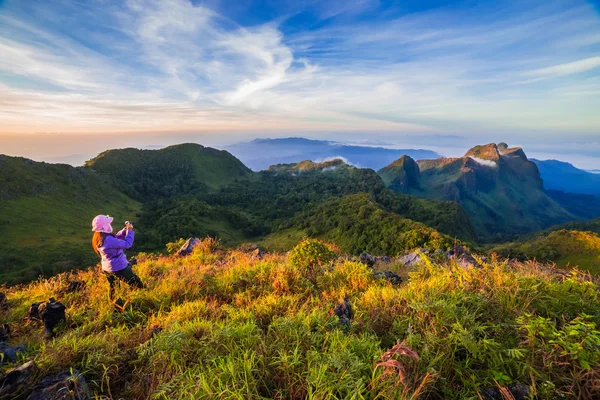 Mujer joven tomar fotografías durante la puesta del sol en la montaña con vista al paisaje — Foto de Stock