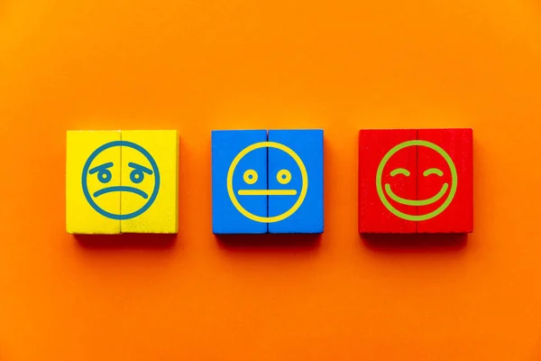 Customer service experience and satisfaction survey concept with facial expressions negative, neutral and positive on wooden cube on table, orange background