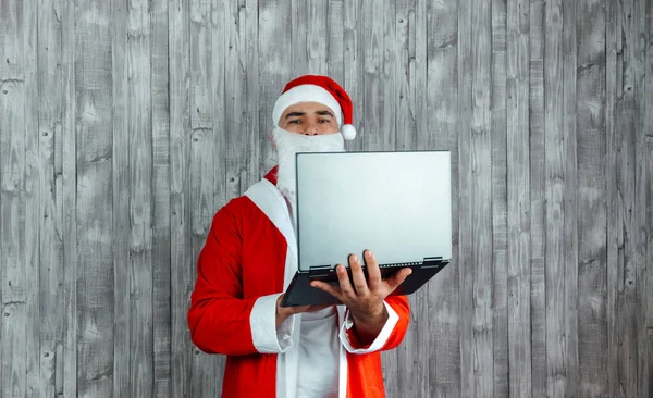 白人年轻人穿着圣诞老人的衣服 手里拿着相机和笔记本电脑 手提电脑网上购物的概念 — 图库照片