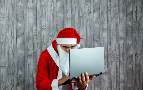 白人年轻人穿着圣诞老人的衣服 手里拿着相机和笔记本电脑 手提电脑网上购物的概念 — 图库照片