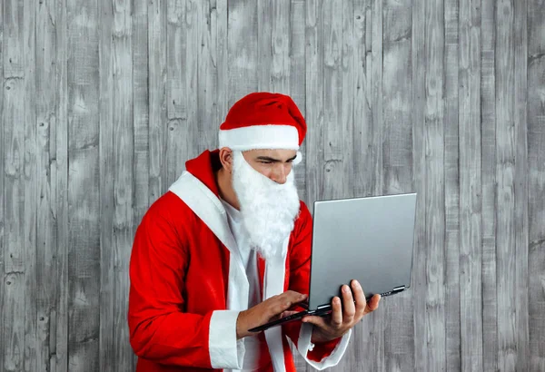 年轻的白人男子穿着圣诞老人的衣服在网上搜索 手提电脑网上购物的概念 — 图库照片