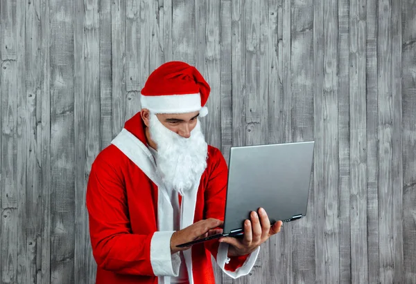 年轻的白人男子穿着圣诞老人的衣服在网上搜索 手提电脑网上购物的概念 — 图库照片