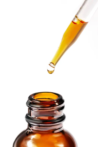 Kozmetik pipeti. Beyaz bir arka planda, Temel Yağ Şişesi 'nin üzerinde kozmetik yağ damlaları.