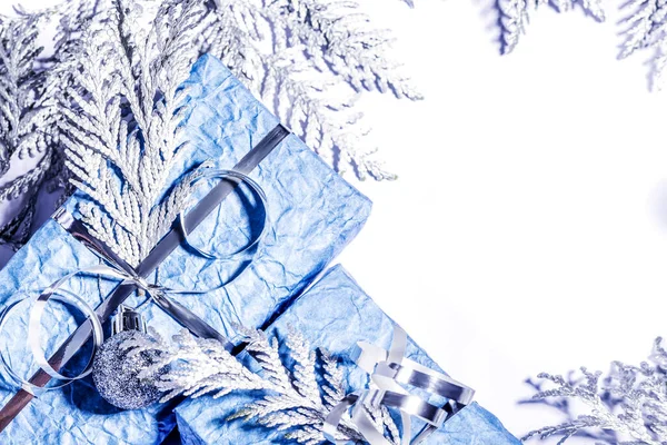 Gümüş thuja dalları, çam kozalakları, mavi ambalajlı hediyeler ve beyaz arka planda festival süsleri olan bir Noel çerçevesi. Genel görünüm, kopyalama alanı olan düz uzanma