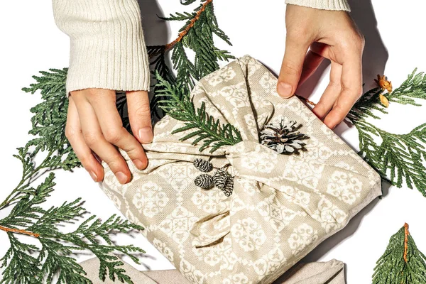 Kız Noel için el yapımı Xmas bej hediye paketini kumaş thuja ve koni ile hazırlıyor. Geleneksel Japon furoshiki tarzında sıfır ziyan hediyesi. Ekolojik konsept çevre dostu dekor xmas.