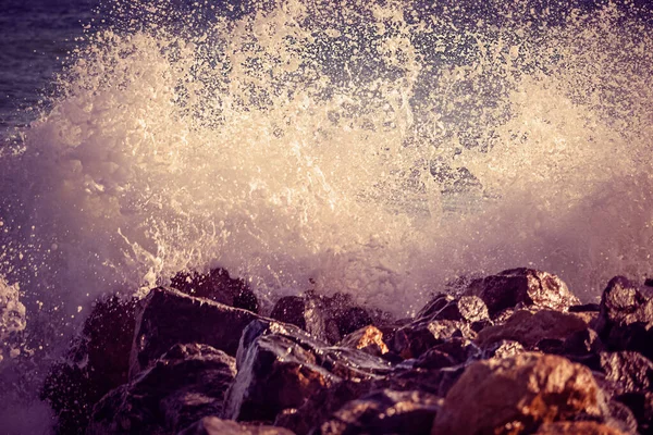 波はビーチで岩に当たり、海の水は日没に噴霧します. — ストック写真