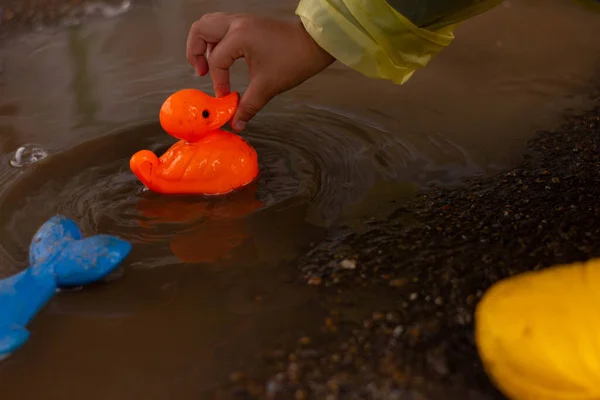 Beautiful girl in denim suit and yellow rubber boots plays with plastic duck and whale in a puddle. High quality photo