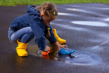Kot takım elbiseli güzel bir kız ve sarı lastik botlar, su birikintisinde plastik ördek ve balinayla oynuyor. Yüksek kalite fotoğraf