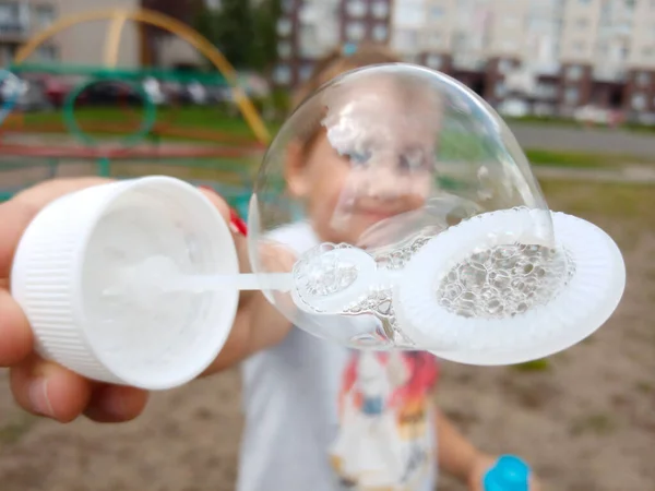 Девушка держит пузырь и смотрит сквозь него на детской площадке — стоковое фото