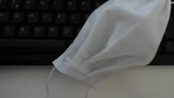 在办公室的黑色键盘上 独自面对面具 白写字台上可处置的白色面罩 — 图库照片