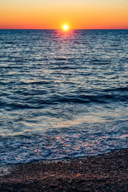 Denizin sakin yüzeyinde gün batımı gökyüzü.