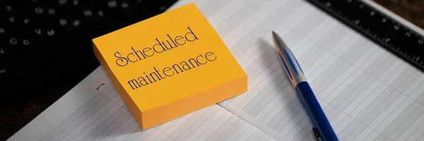 Close-up of a memory stick with the word scheduled maintenance. Selective focus. Calendar scheduler in workplace manager. Ensuring compliance with the preventive maintenance schedule