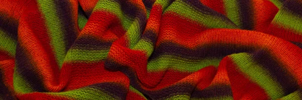 Large handmade merino wool blanket, super chunky yarn, fashion concept. Close-up of a knitted designer blanket in red, green and brown wool. Selective focus