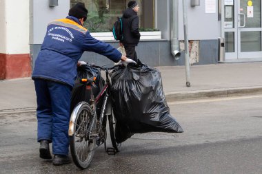 MOSCOW, RUSSIA, 03.27.2021 Şehrin kamu hizmetleri tarafından çöp temizleme. İş kıyafetleri işçisi, çöp dolu bisiklet çantaları taşıyor..