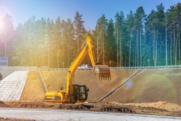 The excavator prepares the site for the construction of the road. Orange construction machinery. Earth-moving heavy equipment on road works