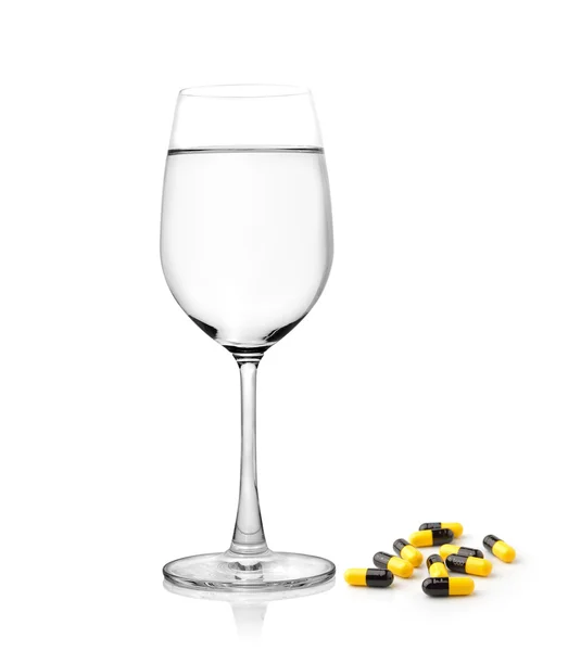 Glas water en pillen capsules geïsoleerd op witte achtergrond — Stockfoto