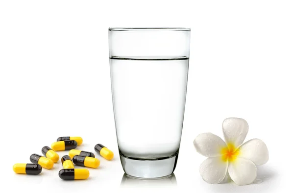 Glass of water pills and Tropical flowers frangipani (plumeria) — Stock Photo, Image