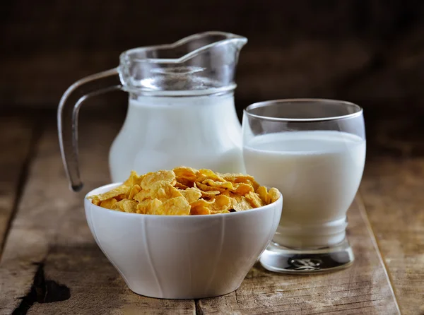 Copos de maíz en tazón y vaso de leche en mesa de madera —  Fotos de Stock