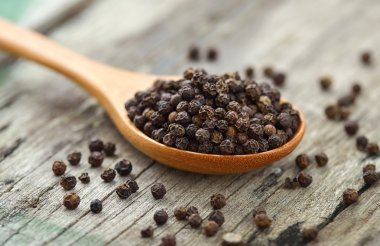 Whole black pepper on wooden spoon clipart