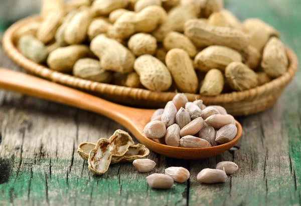 Cacahuètes dans la cuillère à bois et panier sur bois — Photo