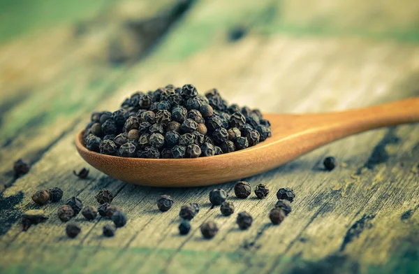 Whole black pepper on wooden spoon — Stock Photo, Image