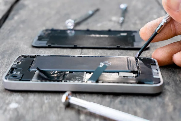 The technician holding a screwdriver a mobile phone repair Closeup inside cell phone with a fixing battery from a broken service shop center on wood table. smartphone repairs maintenance concept.